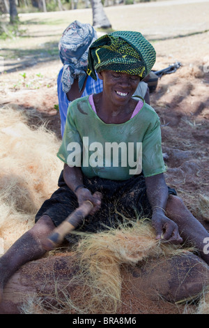 , Kizimkazi Dimbani, Zanzibar, Tanzania. Donna battendo gusci di noce di cocco per produrre filati di cocco, per realizzare corde. Foto Stock