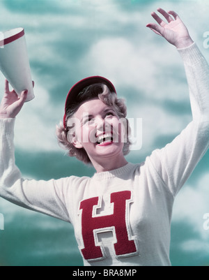 Negli anni quaranta anni cinquanta sorridente ragazza TEEN CHEERLEADER INDOSSANDO GAMMA LETTERA MAGLIONE HOLDING megafono a braccia alzate il tifo Foto Stock