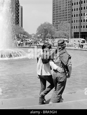 Anni Settanta giovani romantico hippie giovane camminando sotto braccio accanto alla fontana Foto Stock