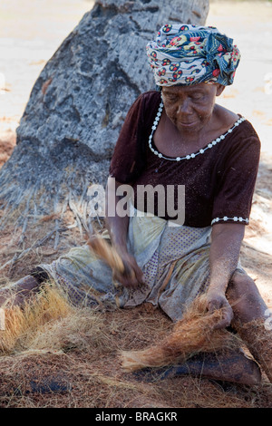 , Kizimkazi Dimbani, Zanzibar, Tanzania. Donna battendo gusci di noce di cocco per produrre filati di cocco, per realizzare corde. Foto Stock