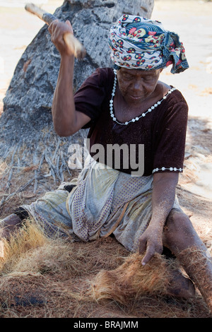 , Kizimkazi Dimbani, Zanzibar, Tanzania. Donna battendo gusci di noce di cocco per produrre filati di cocco, per realizzare corde. Foto Stock