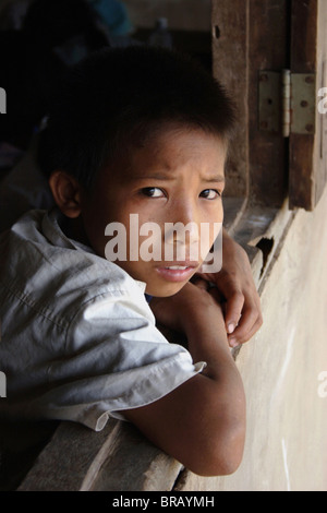 Un 9 anno vecchio ragazzo studente è di guardare al di fuori di un mattone finestra in aula in una scuola primaria in Laos comunista. Foto Stock