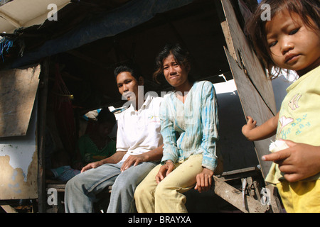 Un uomo e una donna a sedersi in un vicino di casa mentre una ragazza mangia un uovo sodo per colazione in Kampong Cham, Cambogia. Foto Stock