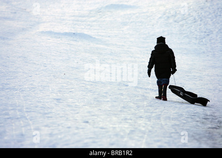 Un ragazzo tirando una slitta fino alla cima di una collina nella neve. Foto Stock