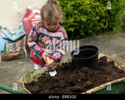Un bambino di sei anni ragazza caucasica riempire una pentola con il compost pronto per piantare in giardino Foto Stock