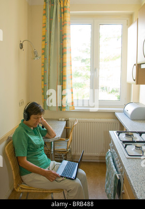 Una donna con un netbook e la cuffia in una cucina Foto Stock