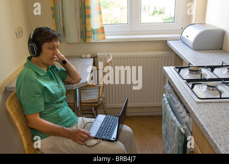 Una donna con un netbook e la cuffia in una cucina Foto Stock
