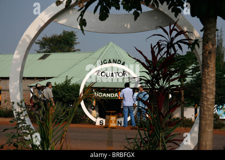 Equatore attraversamento su strada Masaka, Uganda, con negozi e turisti in background. Foto Stock