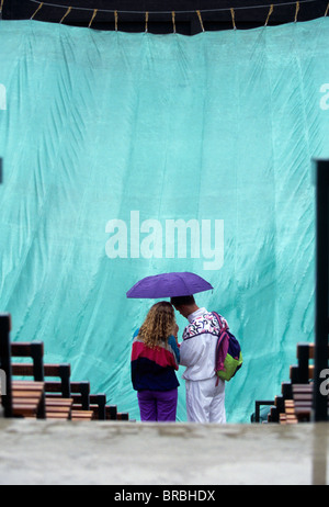 Due spettatori riparo sotto ombrello come la pioggia smette di giocare al torneo di tennis Foto Stock