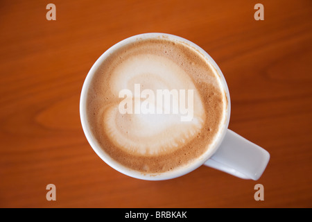 Parte superiore verso il basso di una tazza di caffelatte caffè con una forma di cuore in schiuma sulla parte superiore di una tavola di legno del fondo da sopra. Amore il concetto di caffè Foto Stock