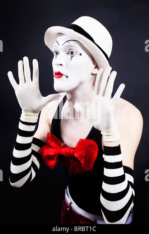 Mime con fiocco rosso ina cappello bianco e guanti a strisce su sfondo nero Foto Stock