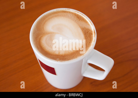 Mug tazza di caffelatte caffè con una forma di cuore nella schiuma sulla parte superiore di un legno marrone dalla tabella di cui sopra. Inghilterra, Regno Unito, Gran Bretagna. Foto Stock