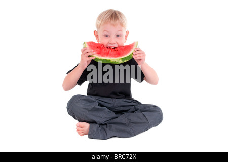 Piccolo Ragazzo seduto sul pavimento tenendo un grosso morso da un cocomero Foto Stock