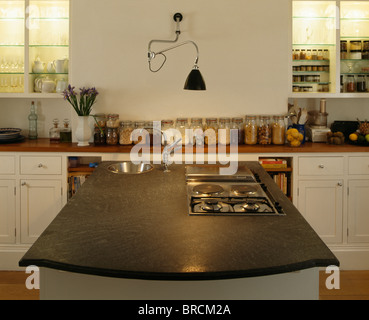 Piano di cottura inset in isola con unità di corian nero piano di lavoro nella moderna cucina bianca con parete-lampada sopra giare di archiviazione sul piano di lavoro Foto Stock