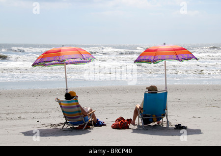 Coppia matura rilassante sulla spiaggia seduti sotto ombrelloni colorati. Foto Stock
