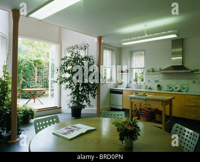 Tall houseplant accanto a aprire le porte del patio in ben illuminato casa cittadina moderna cucina sala da pranzo Camera con legno chiaro tabella Foto Stock