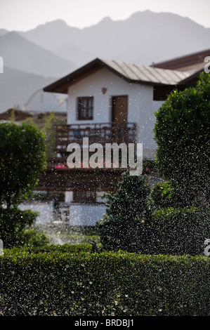 Un sacco di gocce di acqua su un versata prato verde e case di Misty e le montagne sullo sfondo Foto Stock