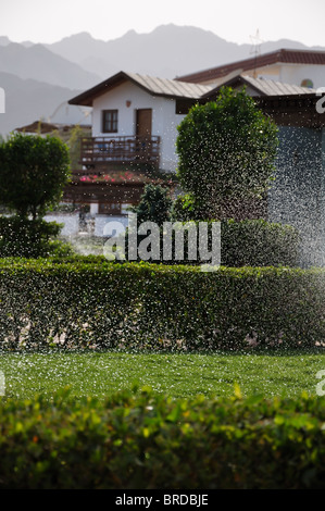 Un sacco di gocce di acqua su un versata prato verde e case di Misty e le montagne sullo sfondo Foto Stock