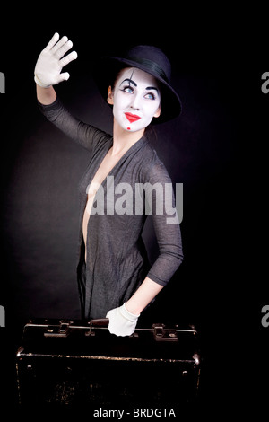 Femmina mime in guanti bianchi con una valigia, dire addio su sfondo nero Foto Stock