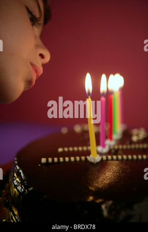 Bambina soffiando compleanno torta al cioccolato candele in una riga su sfondo rosso Foto Stock