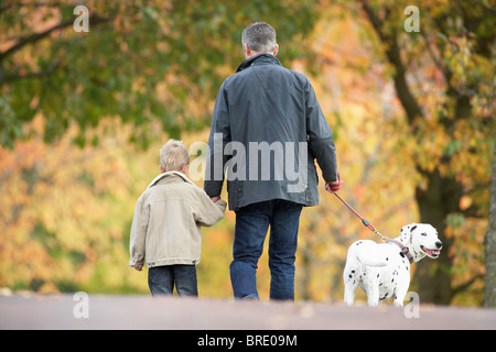 Uomo con figlio giovane cane a piedi attraverso il parco di autunno Foto Stock