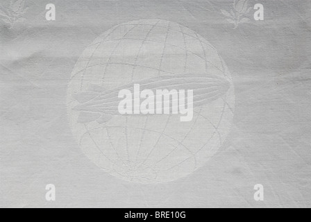 German Zeppelin Shipping Company, un set di tovaglie di seta bianca damask con decorazione della rosa e l'emblema della società nel centro di ogni pezzo nella forma di un airship sopra un globo. Diversi pezzi portano il monogramma 'Sum' del produttore. Il set è composto da un panno da tavolo (105 x 105 cm), cinque guide da tavolo (85 x 45 cm), dieci tovaglioli grandi (60 x 60 cm.) e quattro tovaglioli più piccoli (50 x 50 cm). Anche un tovagliolo di lino con una 'Z' sopra un dirigibile nel centro (58 x 40 cm). Il numero 130 per l'aeronave LZ 130, 'Graf Zeppelin II' è tessuto nei quattro tovaglioli più piccoli. Th, Foto Stock