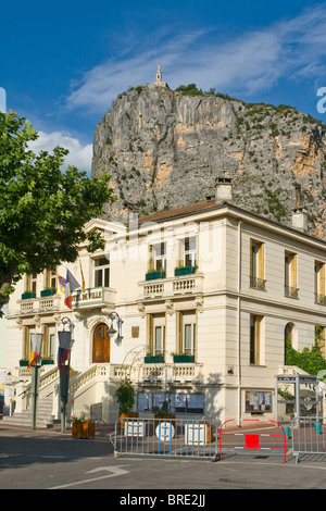 Hotel de Ville in Castellane, Alpes de Haute Provence, Francia, con la cappella di Notre Dame du Roc alta sulla scogliera dietro Foto Stock