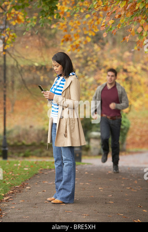 Ragazza adolescente effettuare chiamate sul telefono cellulare con il mio ragazzo a correre verso di lei in background Foto Stock
