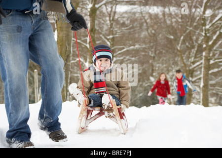 Padre tirando i bambini sulla slitta attraverso il paesaggio invernale Foto Stock