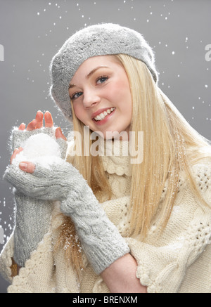 Ragazza adolescente indossare caldo abbigliamento invernale e Hat Holding Snowball In Studio Foto Stock