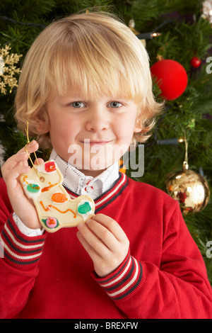 Ragazzo giovane mangiare Cookie nella parte anteriore dell albero di Natale Foto Stock