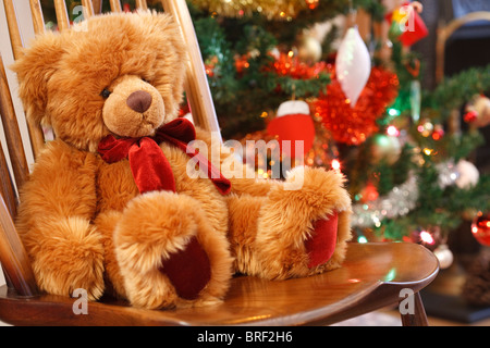 Mercatino di Natale in scena con un orsacchiotto di peluche su una sedia davanti a un albero di natale Foto Stock