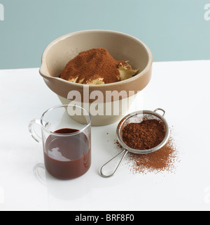 Il budino ciotola con il burro e la polvere di cacao accanto al vetro di cioccolato fuso e il setaccio di cioccolato in polvere Foto Stock