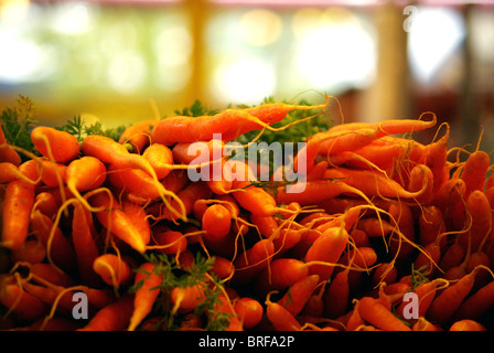 Le carote con la carota verdi accatastati in pile giacente in vendita al mercato degli agricoltori. Foto Stock