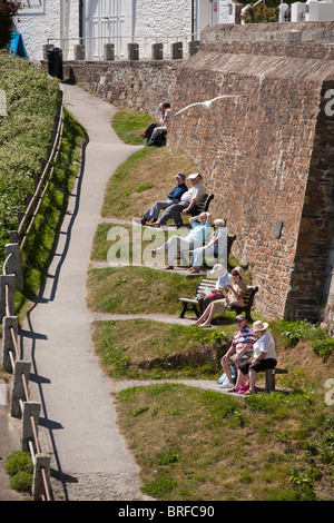 Dieci persone in coppie godendo la vista del porto. Cinque coppie di persone occupano le panchine in un parco stretto al di sotto del seawall. Foto Stock