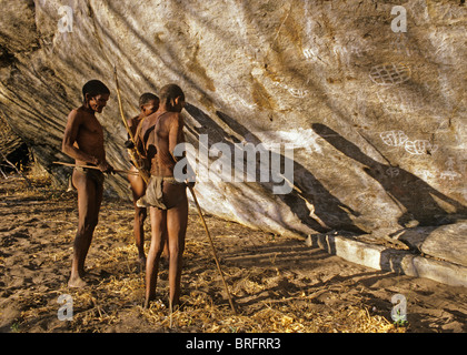 Un gruppo di Boscimani cacciatori esaminare antica arte rock disegni su una roccia a strapiombo faccia Foto Stock