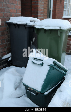 Nero e verde scomparti wheelie fuori un mattone casa con terrazza coperta di neve in attesa di essere raccolti e svuotati dal cassonetto uomini Foto Stock