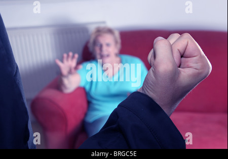 Maschio di pugno alzato volti verso un'anziana donna seduta su un divano a casa Foto Stock