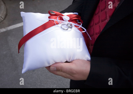 Miglior uomo tenendo gli anelli di nozze sul bianco seta cuscino. Foto Stock