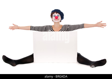 Allegro clown donna seduta sul pavimento e presentando tabellone bianco Foto Stock
