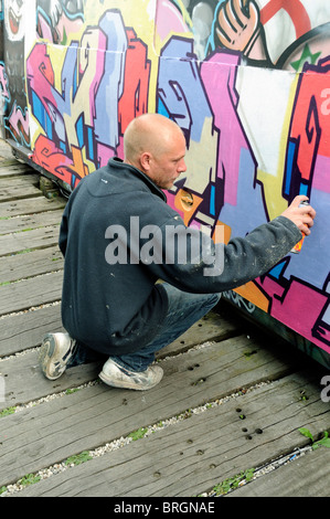 Graffiti artista al lavoro sul lato del tubo in treno, metropolitana di villaggio, Shoreditch Londra Inghilterra REGNO UNITO Foto Stock