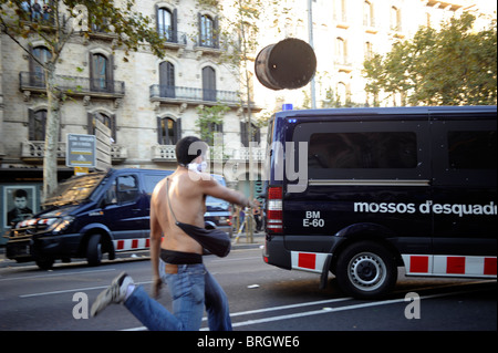 Un attivista anti sistema genera un cestino della spazzatura contro un furgone della polizia durante scontri al centro della città di Barcellona durante lo sciopero. Foto Stock