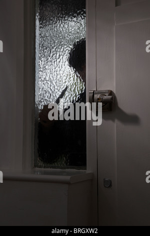 La figura di una persona in possesso di un coltello al di fuori sul vetro opaco finestra mediante una porta anteriore Foto Stock