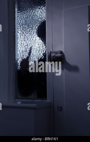 La figura di qualcuno al di fuori di guardare attraverso un vetro opaco finestra, tenendo il coltello Foto Stock