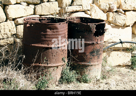 Una coppia di Rusty i fusti di olio contro una parete di pietra arenaria a Gozo Malta off Foto Stock