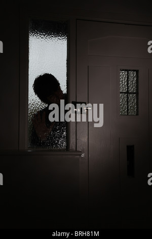 Silhoette di un uomo fa capolino attraverso smerigliati glaas accanto alla porta anteriore Foto Stock