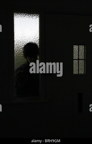Silhouette di un uomo fa capolino attraverso un vetro smerigliato accanto alla porta anteriore Foto Stock