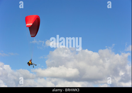 Parapendio in volo con ala rossa / tettoia contro blu cielo molto nuvoloso Foto Stock