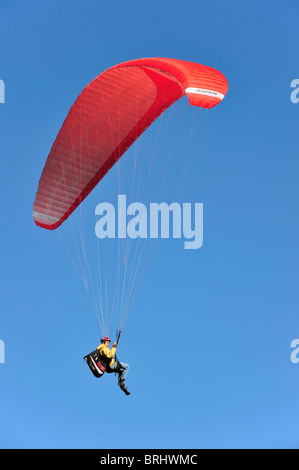 Parapendio in volo con ala rossa / tettoia contro il cielo blu Foto Stock