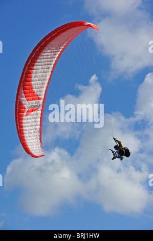 Parapendio in volo con ala rossa / tettoia contro blu cielo molto nuvoloso Foto Stock